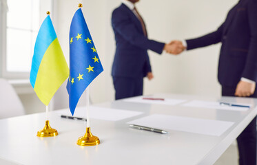 Flags of Ukraine and EU against background of representatives of countries shaking hands. Diplomats...