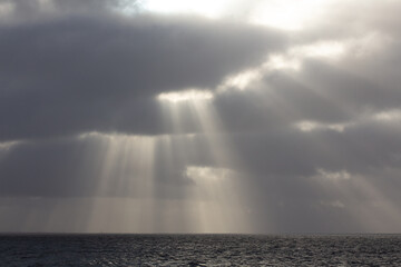 Dramatic clouds in the sky with sun beams over north sea with horizon