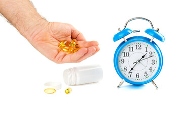 Time to take medicine, a man takes pills, a hand with pills and an alarm clock on the table on a white background.