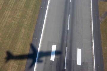 Aircraft shadow after takeoff on ground over airport runway with green grass