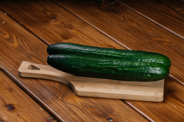 Two green cucumbers lie on a cutting board on the table