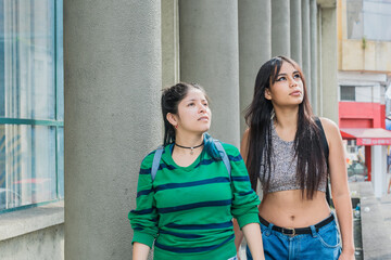 two beautiful latina girls (caucasian and brunette) walking down the street very happy while talking and discussing their dreams and goals for the future. looking at the sky and the tall buildings.