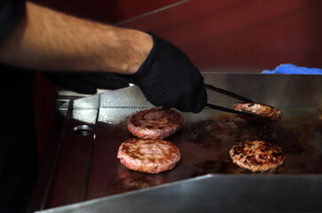 chef preparando hamburguesas a la plancha dándoles la vuelta con un pinza de cocina y guantes de...