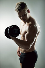 Fototapeta na wymiar Weights before dates. Studio shot of a muscular young man exercising with a dumbbell against a grey background.