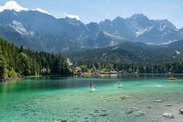 The german mountain lake Eibsee with clear water and people on their stand up paddle boards with...
