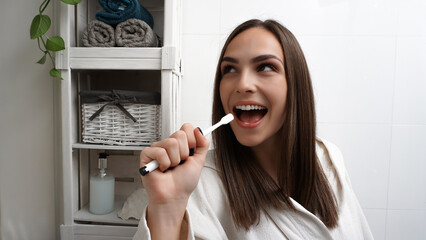 Beautiful young smiling woman singing in the bathroom holding a toothbrush like a microphone. Happy...