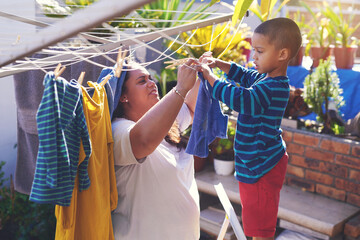 They enjoy spending quality time together. Shot of a mother and son hanging laundry on a washing...