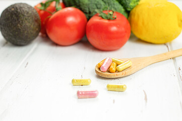 colorful vitamins medicines capsules on wooden spoon with colorful vegetables on background. healthy lifestyle, supplements and vitamins