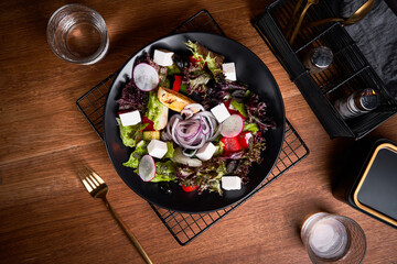Fototapeta na wymiar Fresh greek salad with tomato, radish, onion, bel pepper , olives and feta cheese on black plate, top view, wooden background