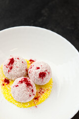 Homemade coconut balls, raw and healthy sugar free rafaello candies. Vegetarian energy sweets recipe. Round tasty dessert in bowl with yellow mango sauce on dark background. Copy space, close up view.