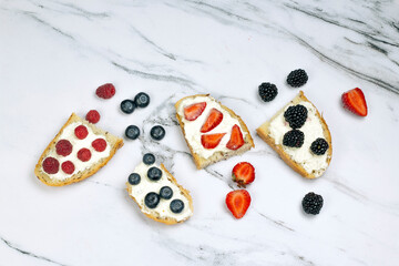 Naklejka na ściany i meble Tasty toast bread with cream cheese, strawberry, raspberry, blackberry and blueberry on white marble background. Morning, breakfast concept, top view, flat lay.