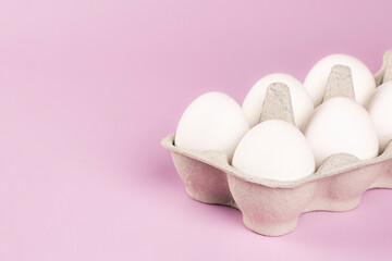 Fresh chicken eggs in egg carton box on pink background. Top view, flat lay with copy space. Natural healthy and organic food concept.