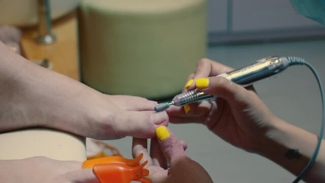Beautician removes old varnish using manicure machine. Removal of old gel. Manicurist woman removes gel shellac polish from client's nails using manicure machine before the pedicure.