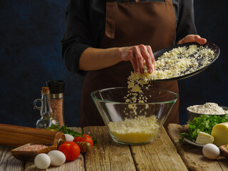 Cooking dishes with grated cheese by the hands of a professional chef on a dark blue background. Lots of products on a wooden table. Restaurant, hotel, cafe, home cooking. Banner.