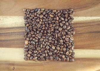 Coffee beans lie on a wooden board in the shape of a square. View from above