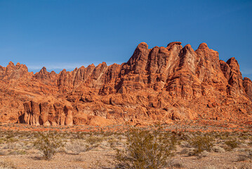 Overton, Nevada, USA - December 11, 2010: Valley of Fire. Landscape with giant red rocks set in battle order line under blue sky. Front dry desert floor with greenish bushes.