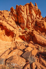 Fototapeta premium Overton, Nevada, USA - December 11, 2010: Valley of Fire. Group of sharp pinned red rocks close together behind heap of rocks with dry bushes on top under blue sky.