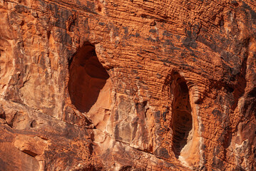 Overton, Nevada, USA - December 11, 2010: Valley of Fire. Closeup of 2 niche0-caves in vertical wall of striped red-rock cliff with black spots.