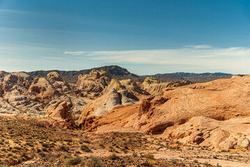 Overton, Nevada, USA - December 11, 2010: Valley of Fire. Wide  red rock landscape with collection of gray rocky stumps under blue cloudscape. Field of dry desert floor with bushes.