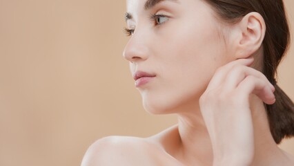 Dark-haired attractive young Caucasian beauty woman turns her head aside and touches jawline on...