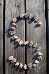 Letter S from small river stones. Capital letter on wooden background. Stone alphabet.