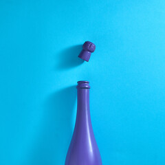 A purple bottle of champagne and a cork on a bright blue background. Text space. Top view. Minimal style.