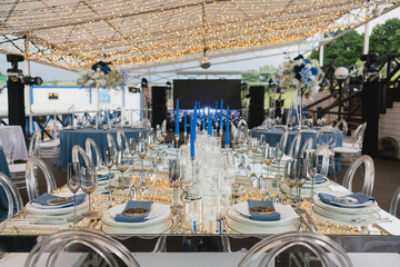 Coziness and style. Modern event design. Table setting at wedding reception. Floral compositions with beautiful flowers and greenery, candles, laying and plates on decorated table.