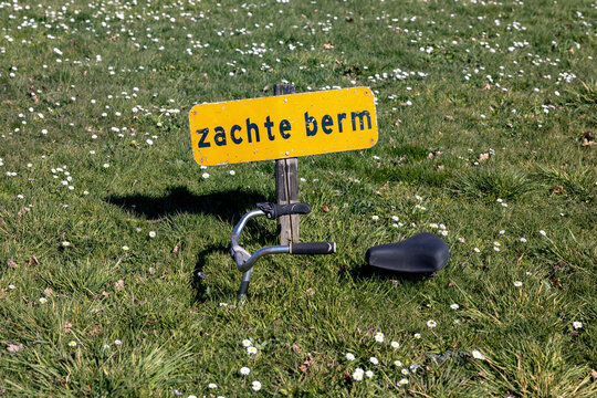 Warning sign says soft roadside in dutch and a sunken bike