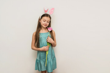 a little girl with long dark hair in the ears of a hare holding a pink tulip, easter concept, easter