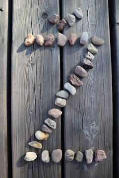 Letter Ž from small river stones. Capital letter on wooden background. Stone alphabet.