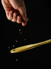 A woman's hand pours peppercorns on a wooden spoon on a black background. Levitation. Minimalism....