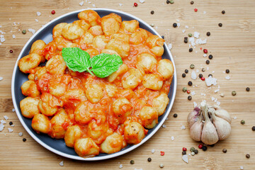 Traditional homemade Italian gnocchi in aromatic tomato sauce served on a decorative plate and garnished with herbs, basil, colored pepper, garlic and pink Himalayan salt. 