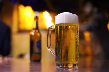 Beer Glass with Foam and Beer Bottle in Background