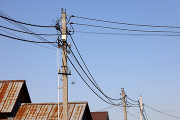Powerline posts with electrical wires and capacitors above old roofs on blue sky background....