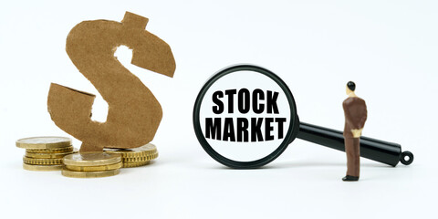 On a white surface, a dollar symbol, a human figure and a magnifying glass with the inscription - STOCK MARKET