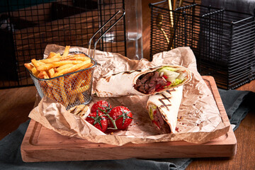Turkish Shawarma with beef and fried with tomatoes on craft paper on wooden plate. Fast food set. Side view