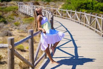 Fototapeta premium African female wearing a beautiful dress on a boardwalk on the beach.