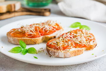 Appetizing sandwich with dried tomatoes and clover and alfalfa sprouts on a plate on the table. Diet organic food. Close-up