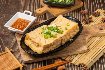 oily tofu in a dish with chilli sauce isolated on wooden board side view on table taiwan food