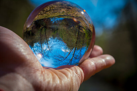 Hand holding glass ball with inverted nature and landscape image