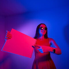 happy girl showing blank paper notebook in neon lights