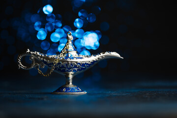 Antique Aladdin's lamp, inlaid with precious stones on a blue background with lights. Arabian...