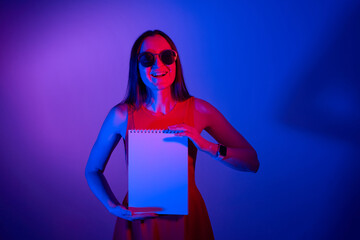 happy girl showing blank paper notebook in neon lights