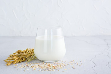 Oat milk in a glass, ears and scattered dry oatmeal on a light table. Alternative plant food. Copy space