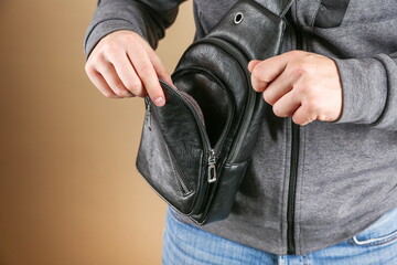 men's leather sling bag is on person close up. man's hands opens the bag close up