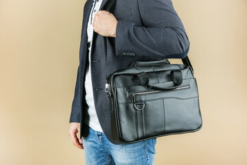 man holds leather briefcase close up,  on brown background. Men's leather bag, studio photo shot