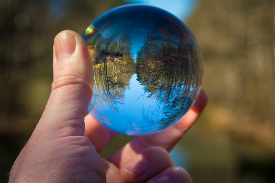 Hand holding glass ball with inverted nature and landscape image
