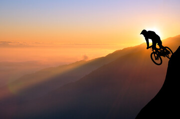 Silhouette of a mountain biker enjoying downhill during the sunset. Cyclist silhouette on the hill beautiful colorful sky and clouds in the background.