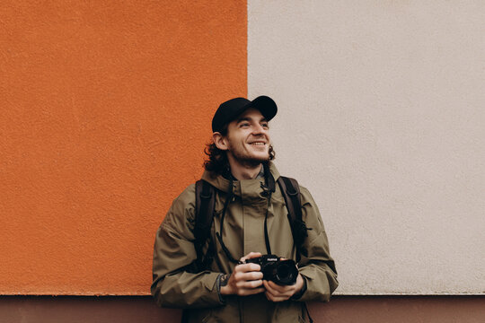 Portrait of a young male photographer with a camera taking pictures or videos on the street. Handsome young man with a professional camera on a background of a colored wall