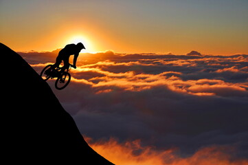 Silhouette of a mountain biker enjoying downhill during the sunset. Cyclist silhouette on the hill beautiful colorful sky and clouds in the background.